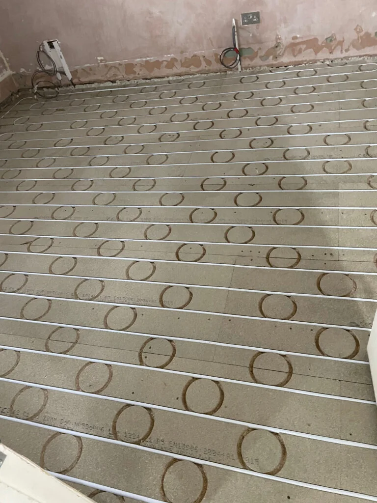 Underfloor heating pipes laid in grooved floor panels