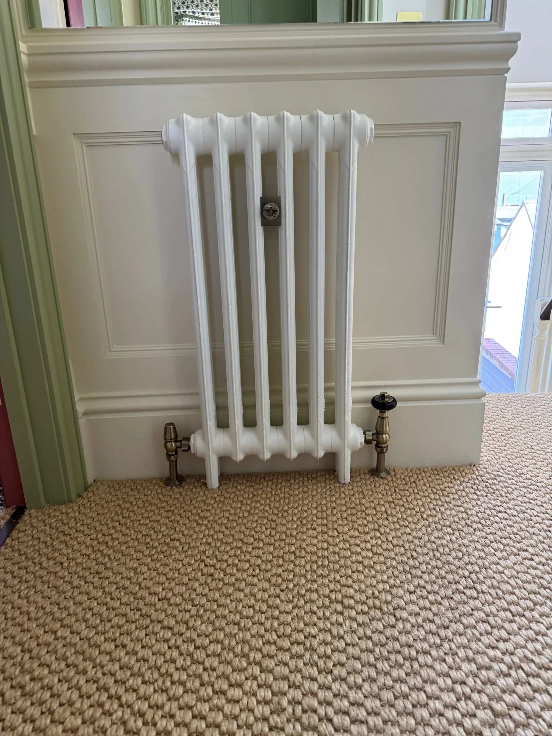 White column radiator with valves beneath a mirror